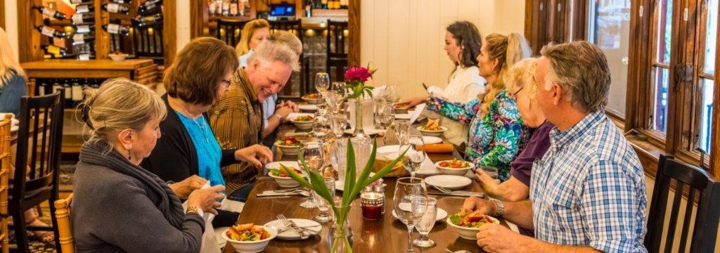 Nine patrons sit at a restaurant table eating salads.